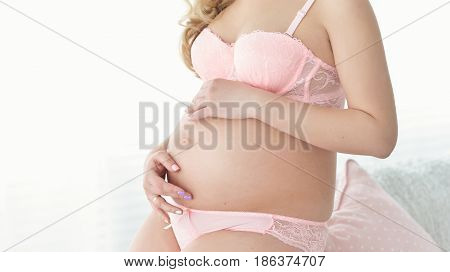 pregnant woman in a pink underwear Hands hold Belly