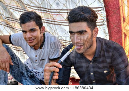 Bandar Abbas Hormozgan Province Iran - 16 april 2017: Two young people are resting in the shade under a fabric canopy one of them is smoking a hookah.