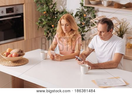 Incurious to our relationships. Addicted incurious involved couple sitting at home and using smartphones while ignoring each other