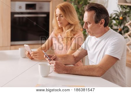 Do not care about our future. Obsessed modern careless couple sitting at home and using smartphones while paying no attention to each other