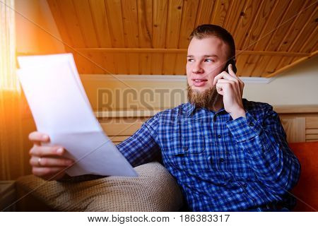 Discussing That Document. Serious Mature Man Holding Paper And Talking On The Mobile Phone While Sit