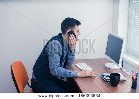An office worker works at a computer in the office and takes an order by phone. Office concept with working environment.