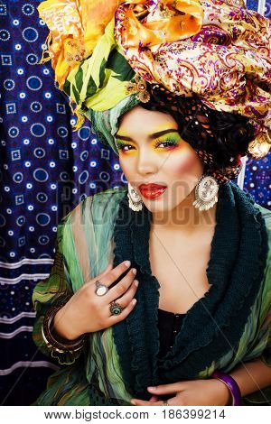 beauty bright woman with creative bright make up, many shawls on head like cubian, ethno look closeup