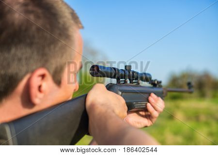 The man takes aim at the target with a sniper strikeball rifle. Selective Focus. Blue sky.