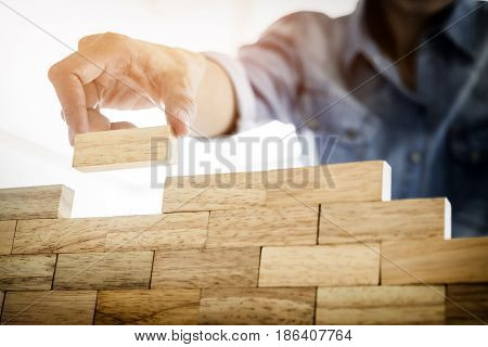 Hand Of Engineer Playing A Blocks Wood Tower Game (jenga) On Blueprint Or Architectural Project Conc
