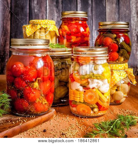 Jars with marinated food and raw vegetables on cutting board.