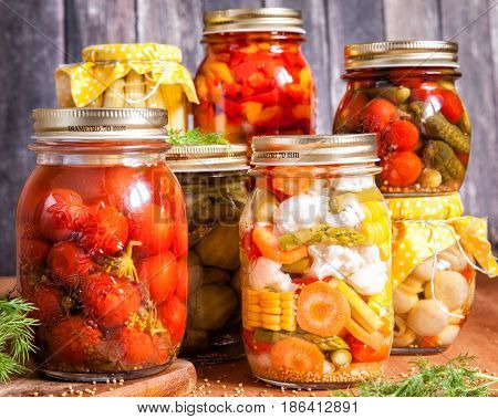 Jars with marinated food and raw vegetables on cutting board.