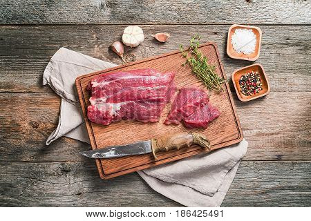 Raw roastbeef meat cut with hyme and garlic and knife on cutting board over old  wooden background, top view