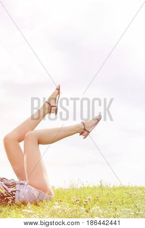 Low section of woman with feet up lying on grass against sky