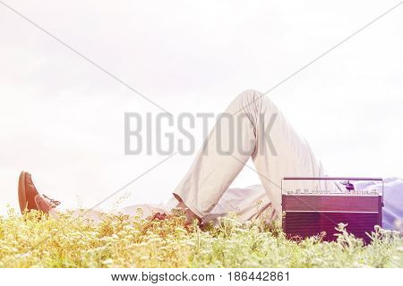 Low section of man lying by vintage radio on grass against clear sky