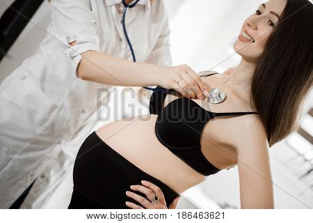 Female Medicine Doctor Holding Stethoscope To Pregnant Woman Standing For Encouragement, Empathy, Ch