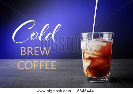 Pouring milk into glass with cold brewed coffee on color background