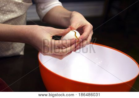 child cracking white egg over orange bowl
