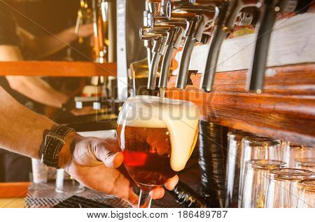 Bartender hand pouring draught beer to glass from a pub tap