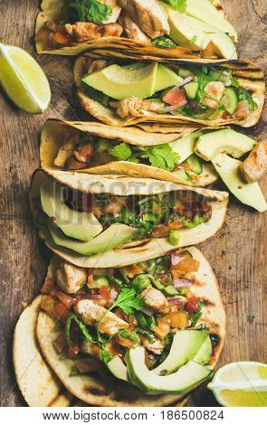 Tacos with grilled chicken, avocado, fresh salsa and limes over rustic wooden background, top view. Healthy low carb and low fat lunch or food for company. Dieting and weight loss concept