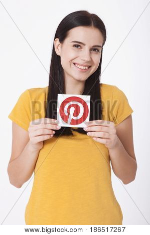 KIEV, UKRAINE - AUGUST 22, 2016: Woman hands holding Pinterest icon printed paper close up. Is photo sharing website.