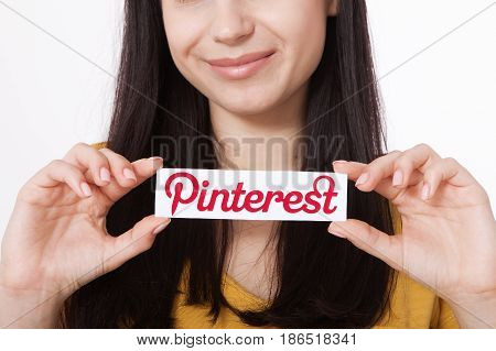 KIEV, UKRAINE - AUGUST 22, 2016: Woman hands holding Pinterest ilogotype icon printed paper close up. Is photo sharing website.