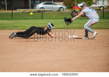 White uniform softball infielder waiting to tag diving black uniform runner.