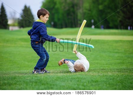 Preschool boys fighting with toy swords in park