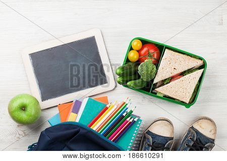 Lunch box with vegetables and sandwich on wooden table. Kids take away food box and school supplies. Top view with chalkboard for your text