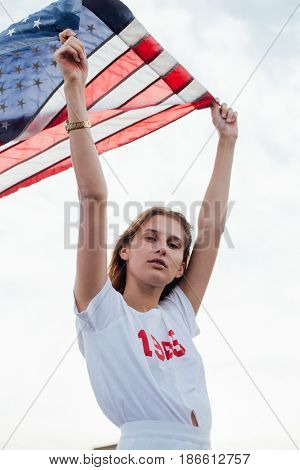 Young caucassian woman holds up american flag high up in the sky with pride and joy