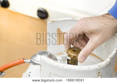 The man's hand unscrews the valve from the gas bottle.