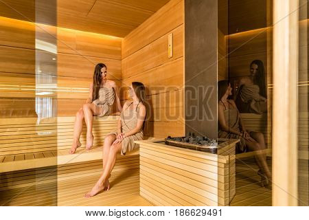 Full length of two female best friends smiling while enjoying the therapeutic effect of a dry sauna in a modern wellness center