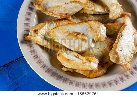 Fried chicken breasts on the plate above blue wooden planks board.