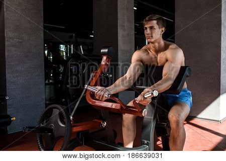 Tense muscles of hands under load. Man doing exercise for biceps in the gym. Work on tell muscles on the simulator. Photos for sporting magazines, posters and websites.