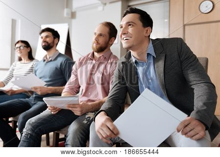 Keep calm and smile. Four colleagues posing in line holding hands on knees while participating in conference