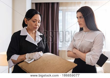 I couldnt clean it. Nice sad unhappy hotel maid standing near her manager and holding a cushion while working in the hotel