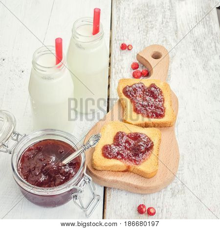 Toasts with strawberry jam and milk for breakfast on white rusric wooden background. Selective focus.