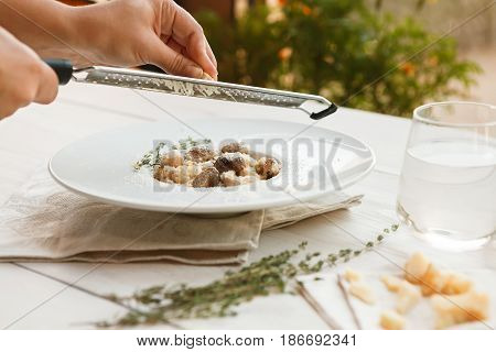 Grating parmesan cheese on wild mushrooms risotto with rosemary. Traditional italian cuisine dish. Restaurant food closeup. Forest fungus with rice. Shallow DOF, selective focus