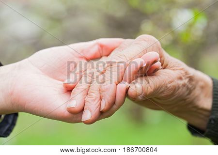 Close up picture of a young woman's hands holding an elderly female's hands