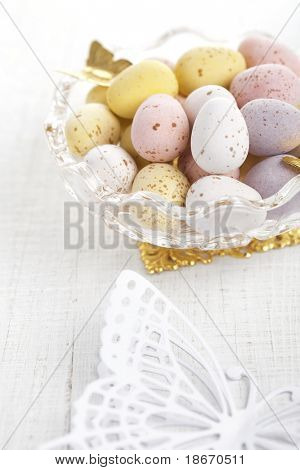 easter chocolate speckled eggs in bowl with paper batterfly on white table, shallow dof