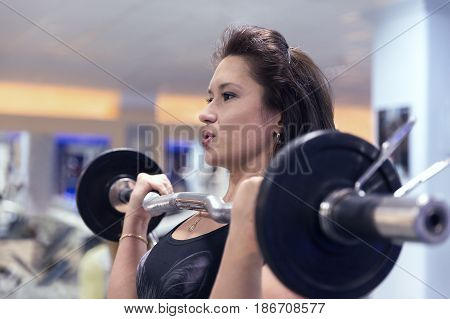Sporty girl raises the barbell in the gym. Build muscles of the arms and chest. Concept of a healthy lifestyle