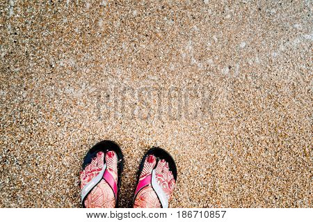 Girl's feet with henna tattoos and sandles. She is standing on a sandy beach probably on a honeymoon vacation