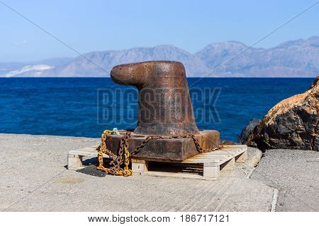 Rusty bitt with a chain on the berth. In the background of sea and mountains.