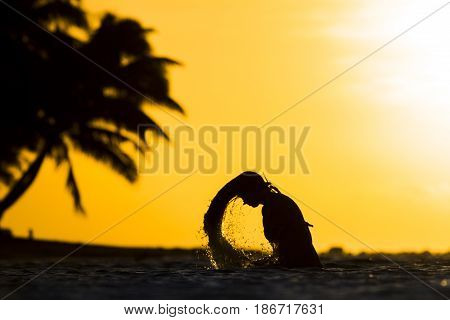 girl throwing water with her hair in the ocean during sunset