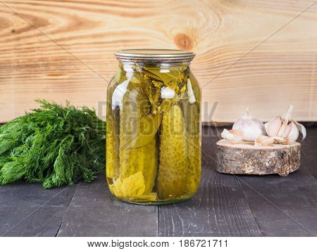 Pickled cucumbers on wooden background. Pickles in glass jar with garlic and fresh dill. Salted cucumber in jar with copy space