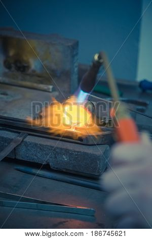 Goldsmith melting gold or silver with gas burner in wedding ring making process