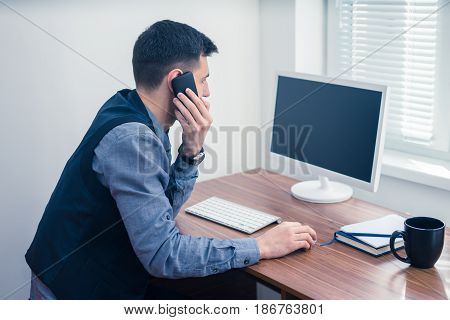 An office worker works at a computer in the office and takes an order by phone. Office concept with working environment.