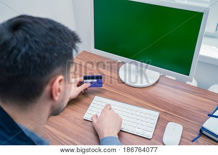 Man in office typing on telephone. computer with Chromakey is on background. Office concept with working environment. Copyspace on screen
