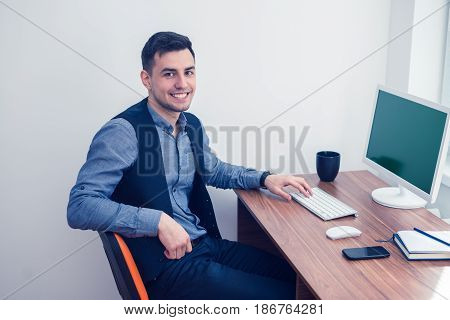 Happy office worker smiling and looking at the camera. He sits at computer with Chromakey. Office concept with working environment. Copyspace on screen