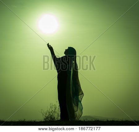 Silhouette Muslim Arabic woman praying with her hands up