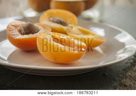 Whole orange apricots with red blush, from above, space for text. Open apricot with stone and leaves. On rustic white wood.