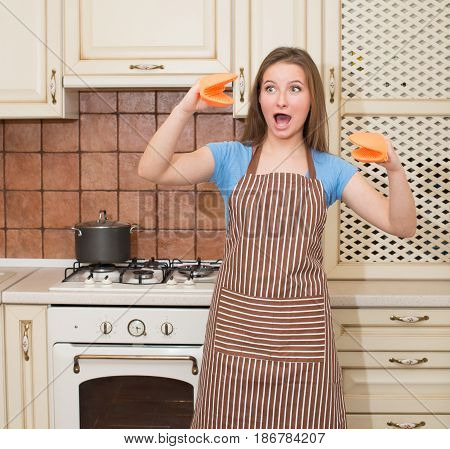 Funny baking cooking woman having fun in her kitchen smiling cheerful wearing apron and oven mitts ready to bake. Beautiful young mixed race woman at home.
