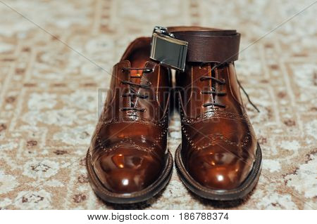 A new pair of tan leather shoes and belt on beige carpet