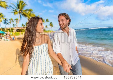 Beach couple happy holding hands on hawaiian holidays in Waiohai beach, Poipu in Kauai, Hawaii, USA. Newlyweds people in love on honeymoon. Asian woman, Caucasian man.