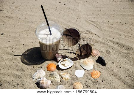 Ice latte on sand with cockleshells and glasses